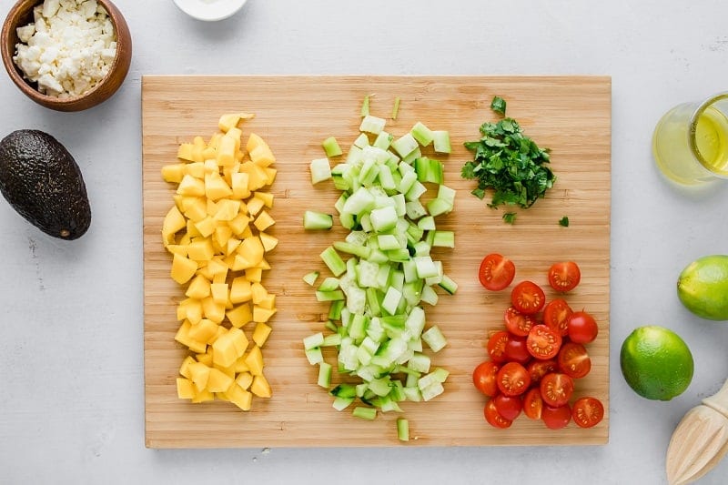 wooden cutting board with diced mango, cucumber, tomatoes