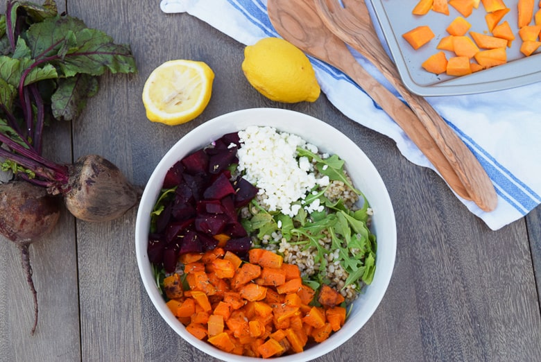 roasted beets and butternut squash salad with arugula and cheese in white bowl