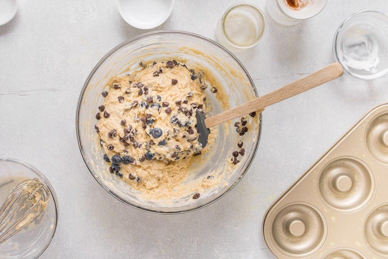 mixing bowl with donut batter and chocolate chips and wooden spatula