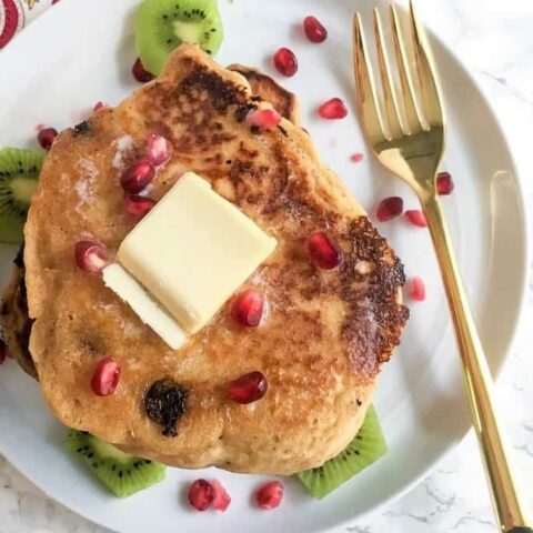 overhead view of gingerbread protein pancakes with slab of butter and pomegranate aerils