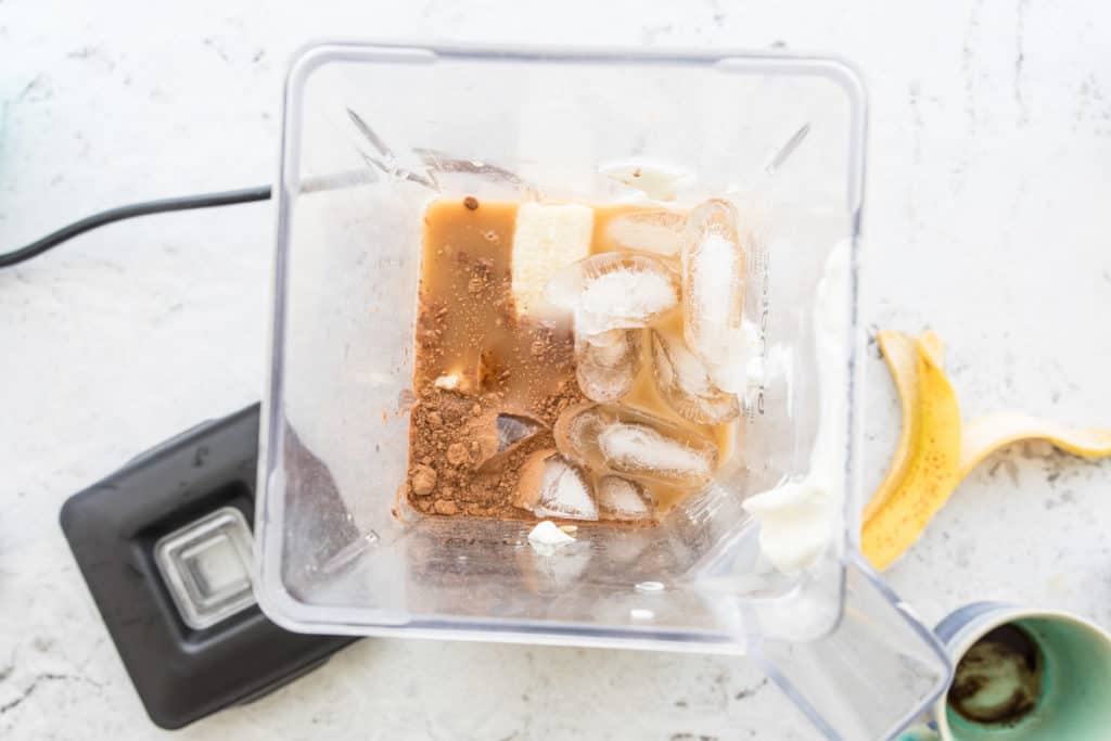 blender with ice cubes, cocoa powder, banana and coffee to make coffee protein smoothie