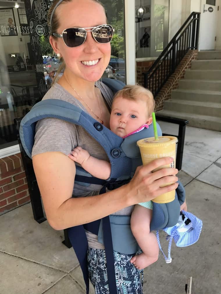 mom holding infant in infant carrier with smoothie in hand