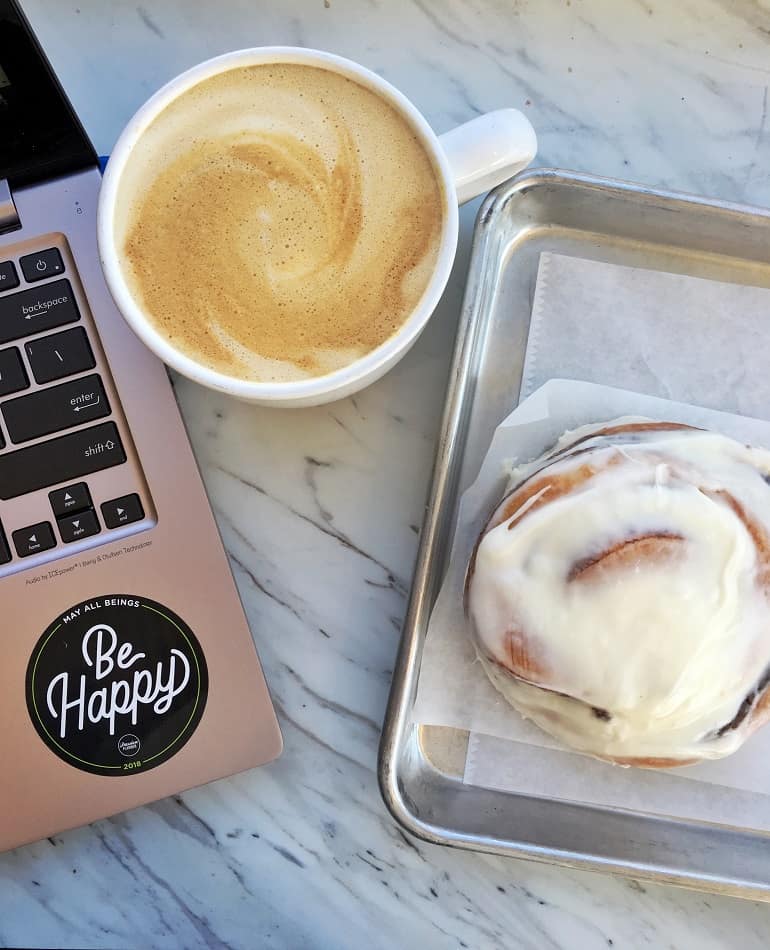 cinnamon bun and latte next to laptop on marble table