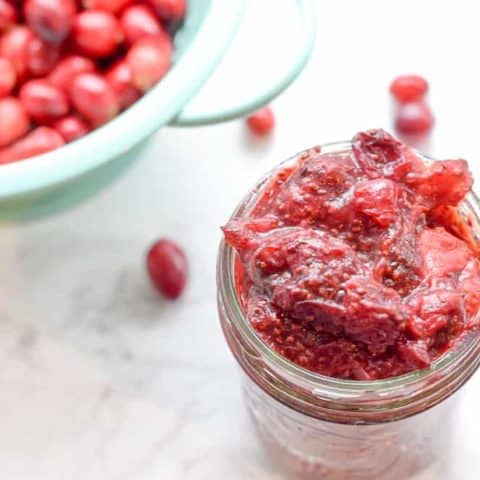 mason jar with cranberry strawberry chia jam and fresh cranberries alongside
