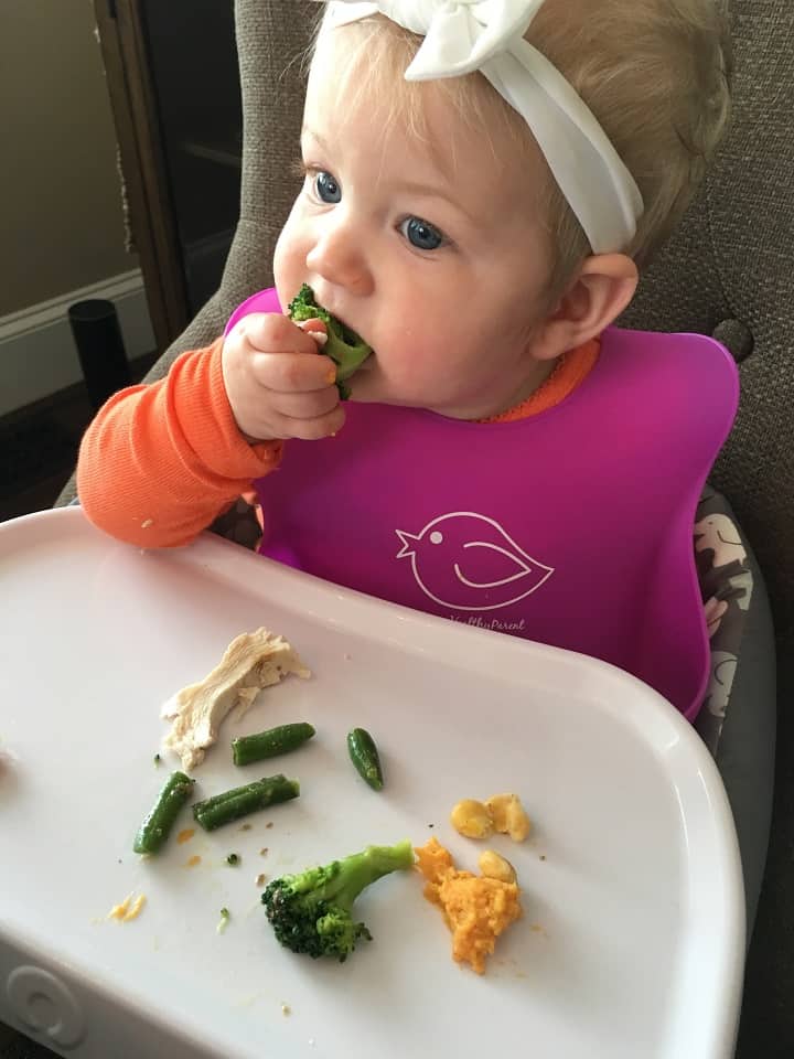baby eating green beans and chicken in high chair