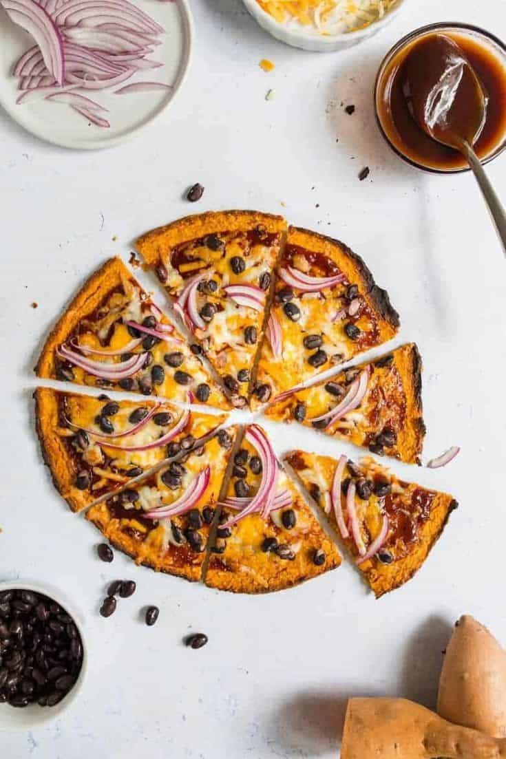 Overhead view of sweet potato pizza crust topped with cheese, black beans and red onions on gray background | Bucket List Tummy