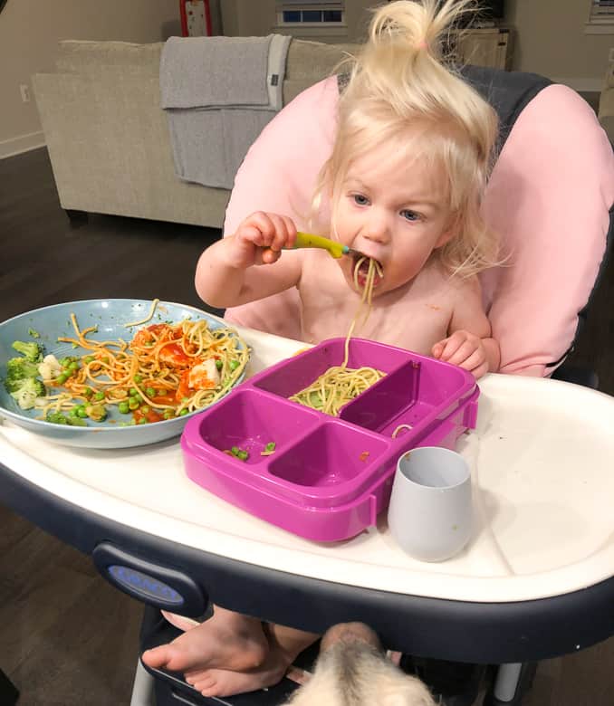 toddler eating spaghetti in a high chair