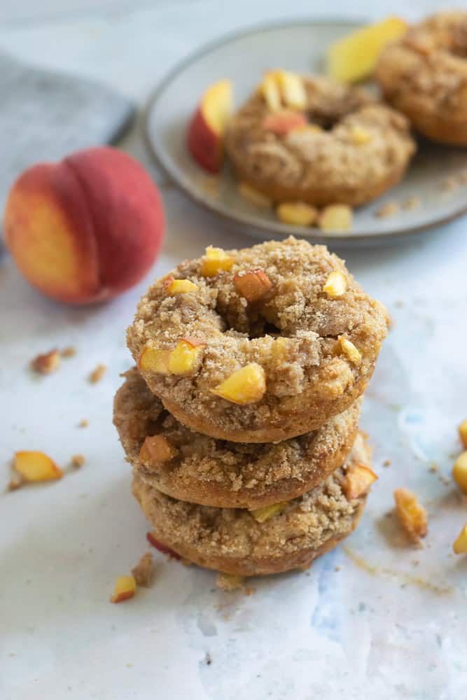 whole wheat donuts stacked with peach crumble topping and peach in background