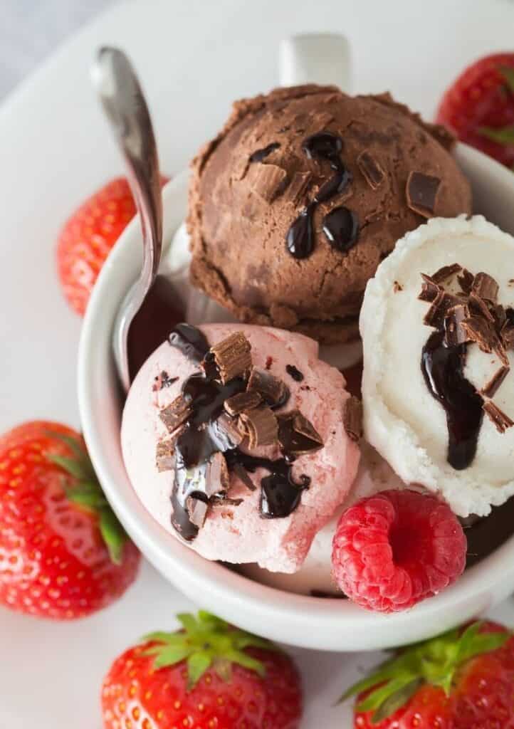 bowl of ice cream with scoop of vanilla, strawberry and chocolate with chocolate sauce and berries on top