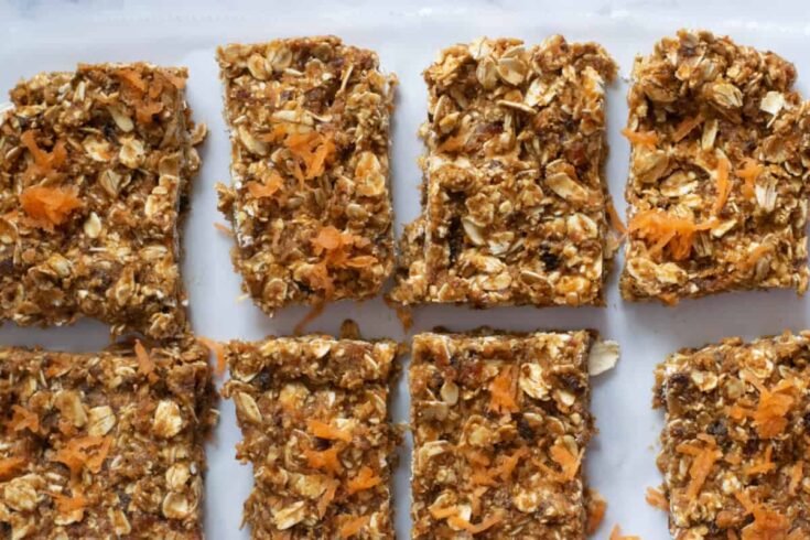 overhead shot of carrot cake no bake bars topped with shredded carrots on parchment paper