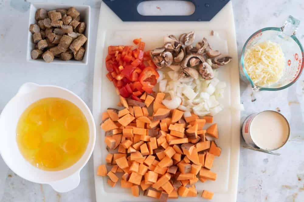 white cutting board with diced sweet potatoes, onions, peppers, mushrooms and other ingredients necessary for breakfast casserole