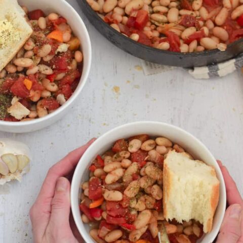 Cannellini Bean Skillet Recipe served in white bowl with bread with person holding bowl
