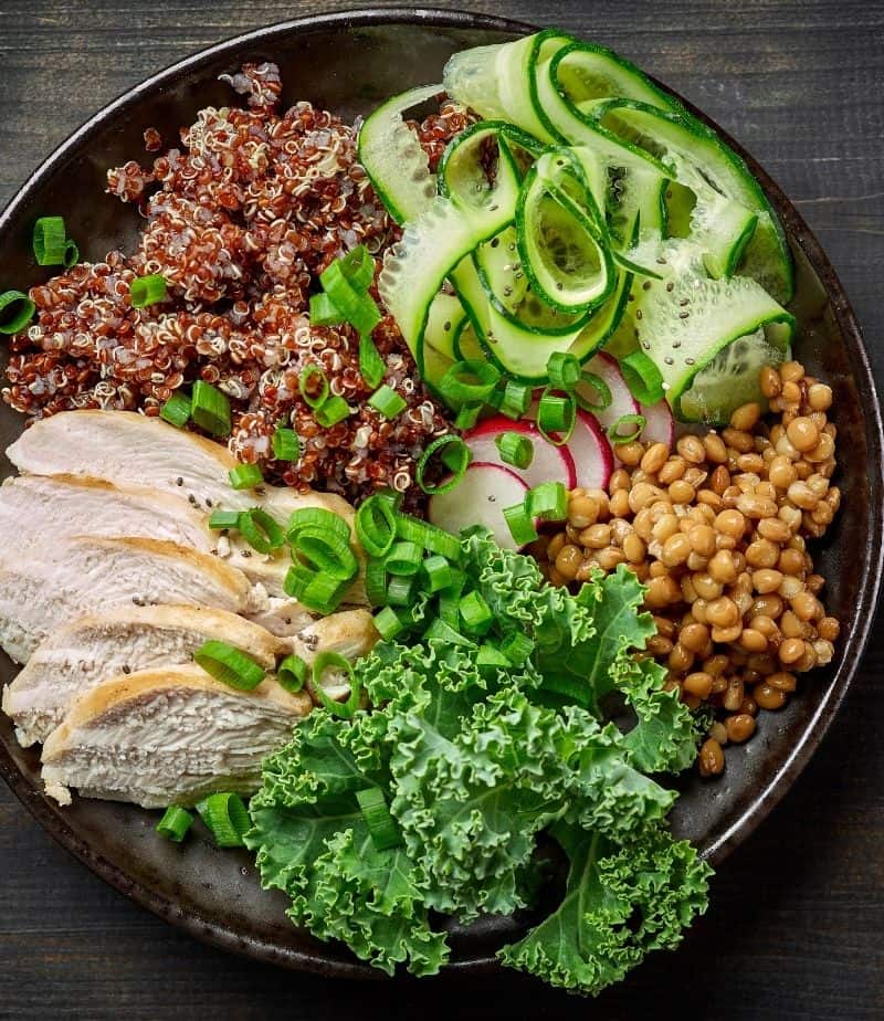 black plate with quinoa, grains, chicken and veggies