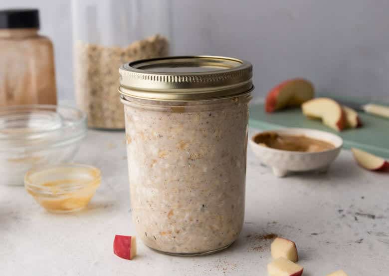 Fall overnight oats in mason jar with cover on top and apples in background