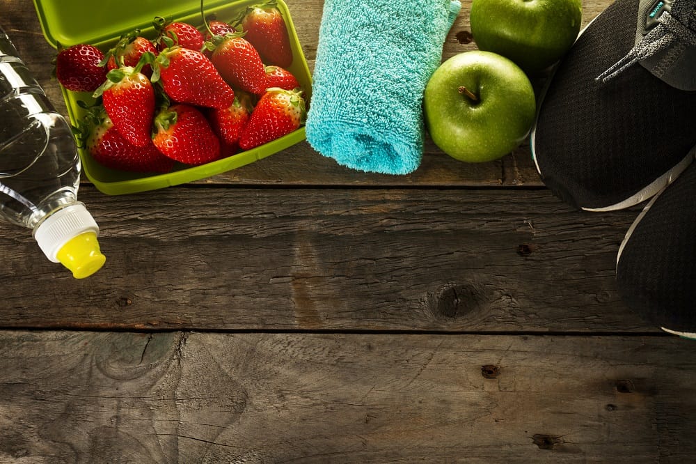 wooden background with strawberries, apple and water bottle post workout