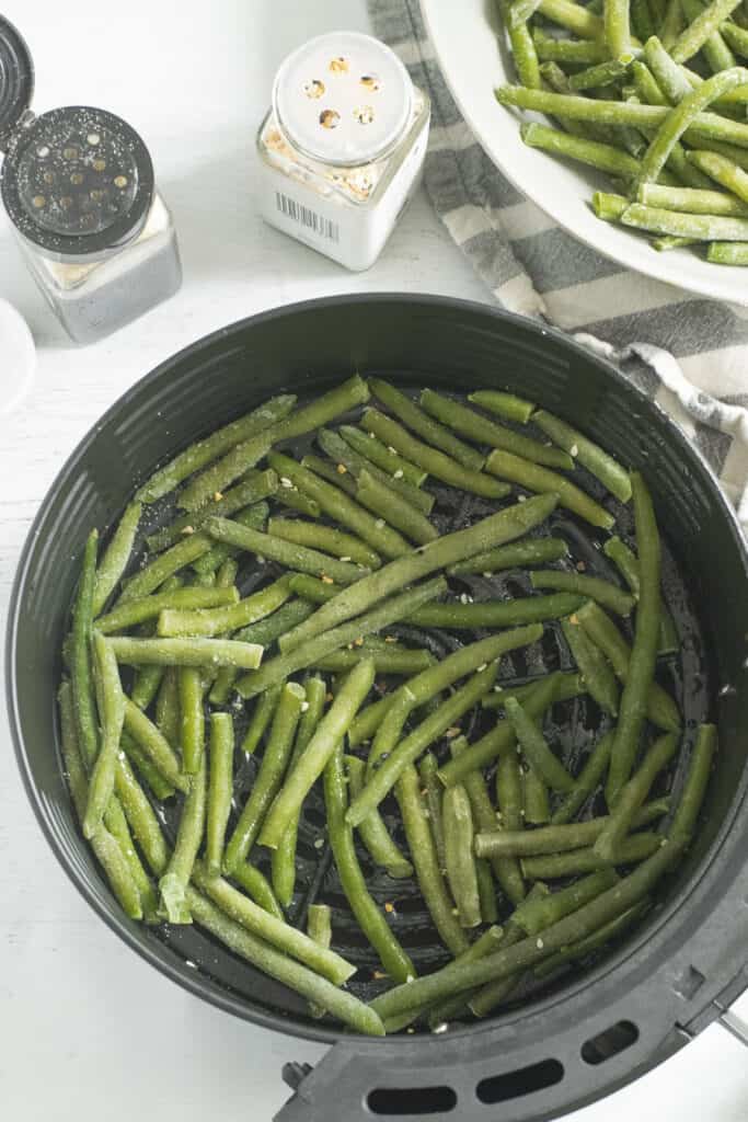 frozen green beans in air fryer tray next to striped napkin