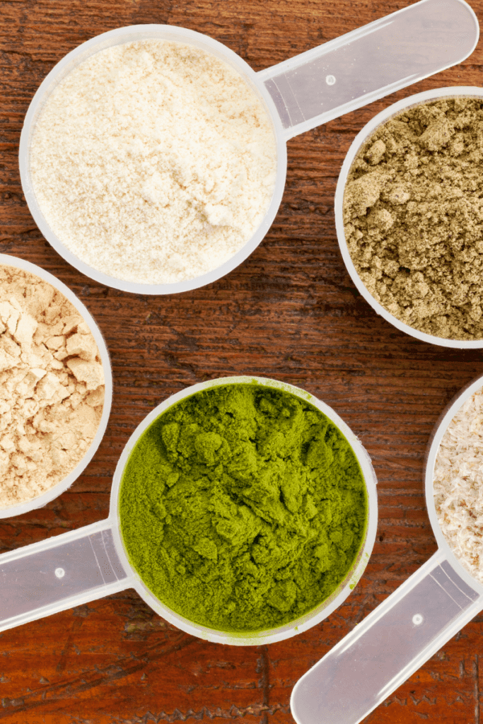 scoops of different protein powders on wooden background