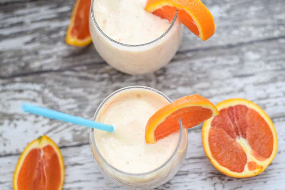 orange and mango smoothie in glasses with oranges on top