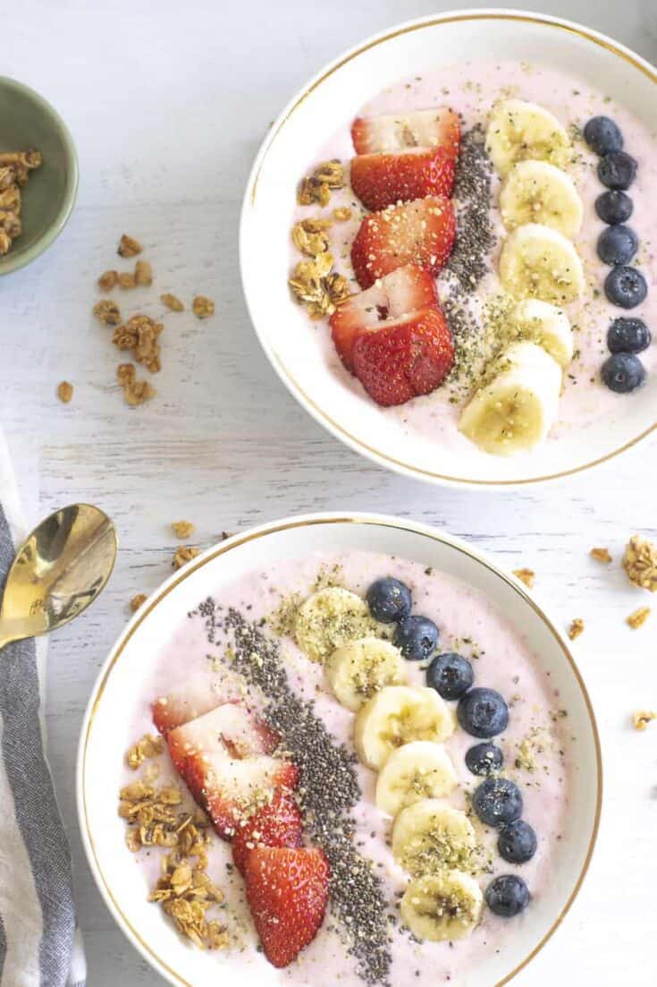 two strawberry banana smoothie bowls with fruit toppings