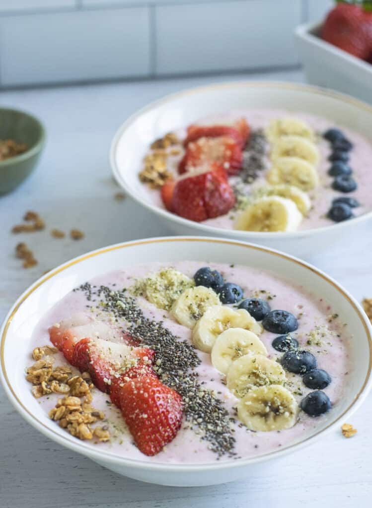 two strawberry and banana smoothie bowls with toppings and granola