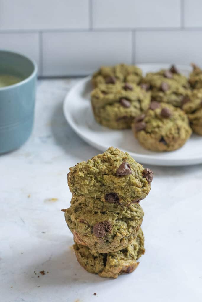 vegan matcha muffins stacked on each other with plate of muffins in background