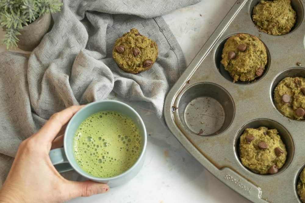vegan matcha muffins on muffin tray next to cup of matcha tea