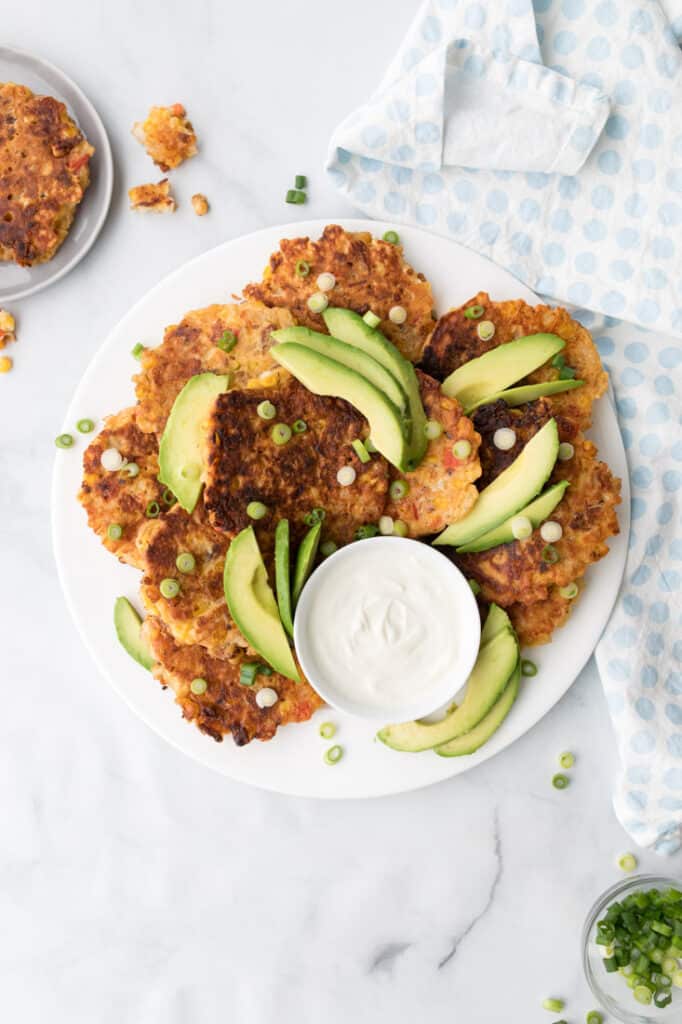 corn and bacon fritters on white plate topped with avocado and green onions
