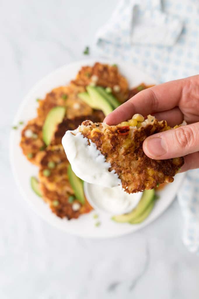 holding up bite of bacon and corn fritter dipped in greek yogurt