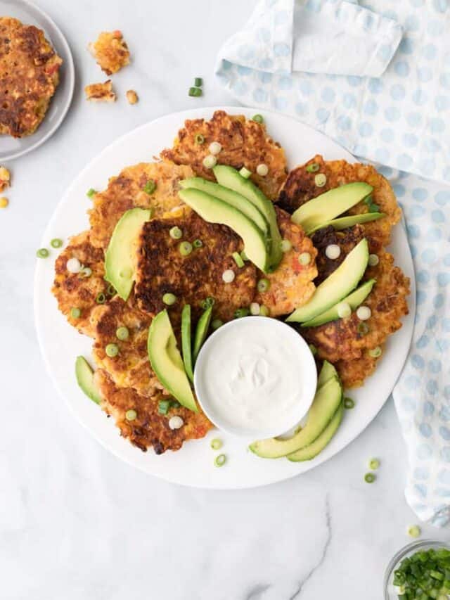 corn and bacon fritters on white plate topped with avocado and green onions