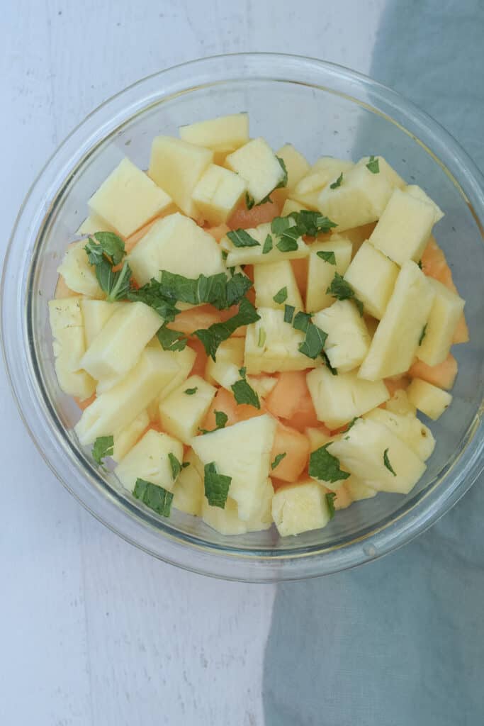 cut up cantaloupe, pineapple and mint in a bowl