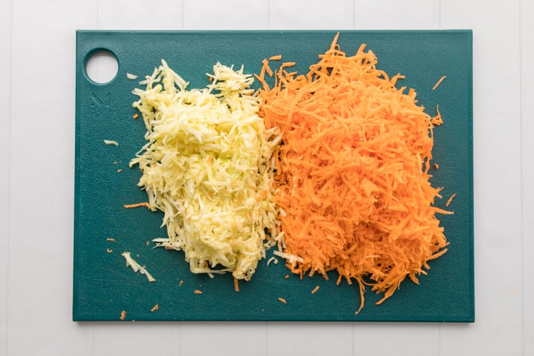 green cutting board with grated sweet potato and zucchini