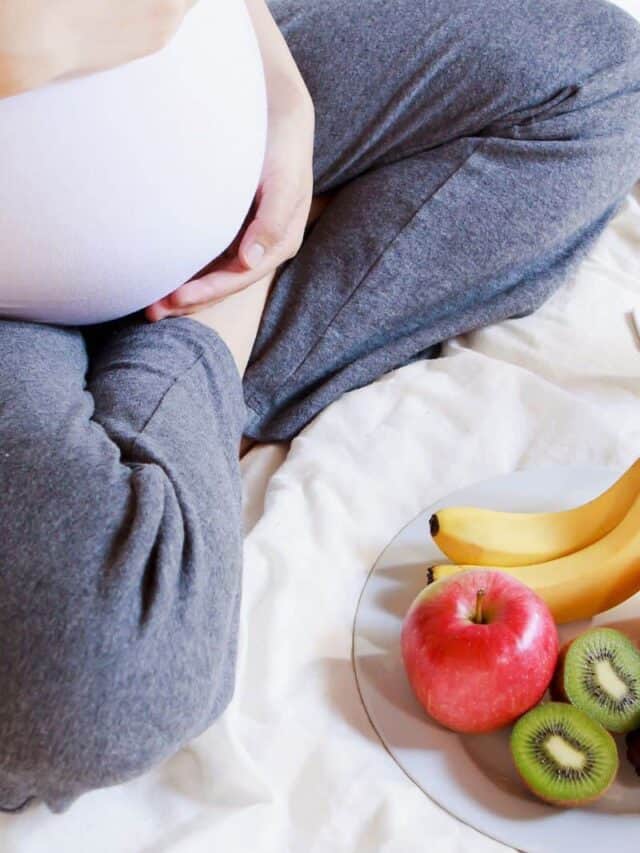 pregnant woman holding belly with bowl of fruit in front of her