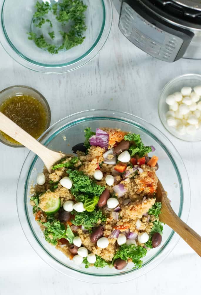 Mediterranean quinoa salad with veggies in clear bowl with salad spoons