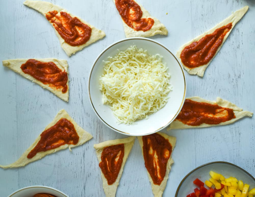 crescent rolls rolled out with pizza sauce and bowl of cheese in the middle