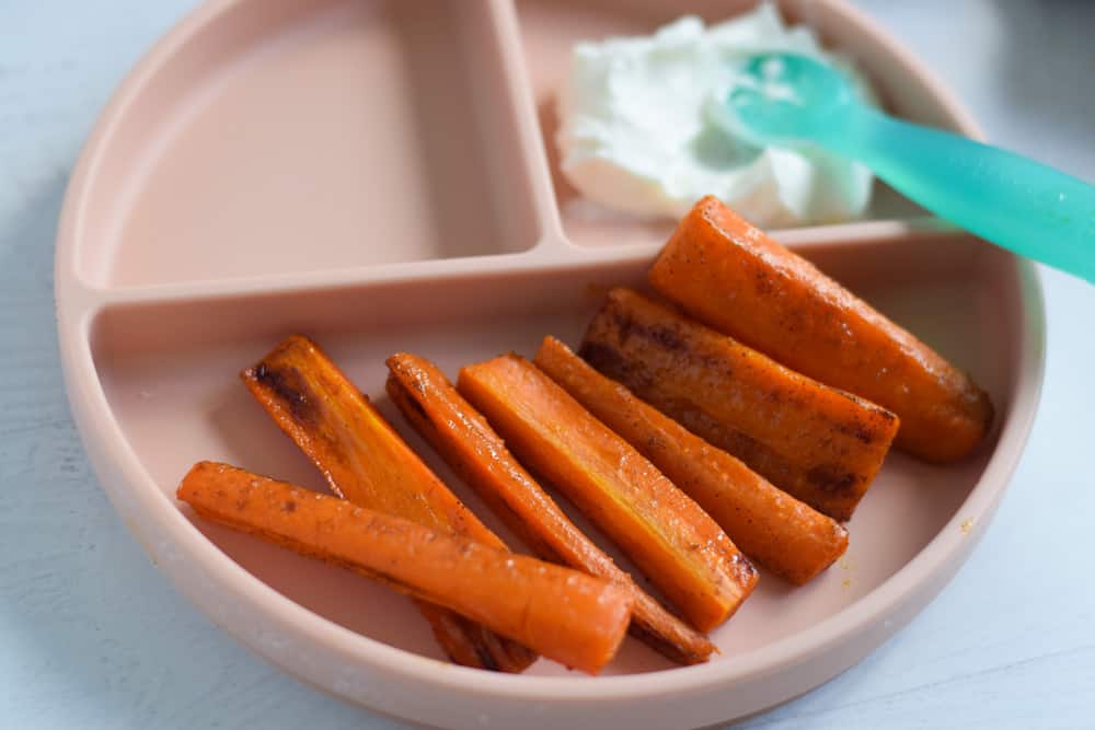 sliced cooked carrots for baby on pink serving plate with yogurt