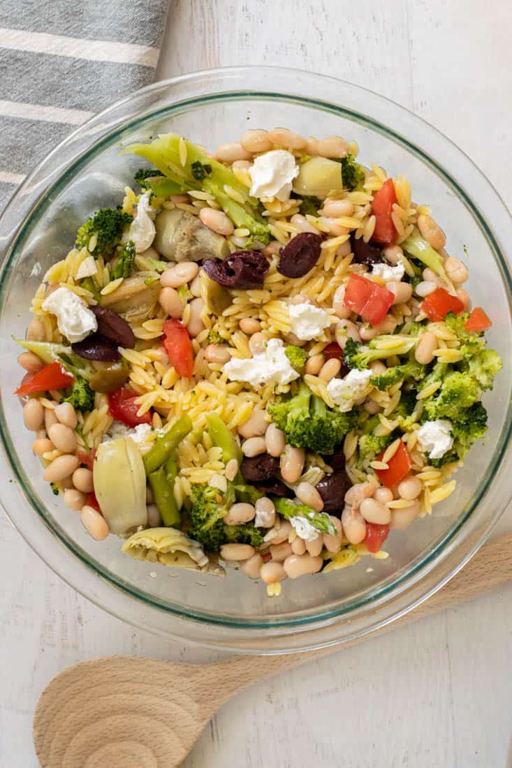 orzo salad with goat cheese, veggies and greens in clear bowl