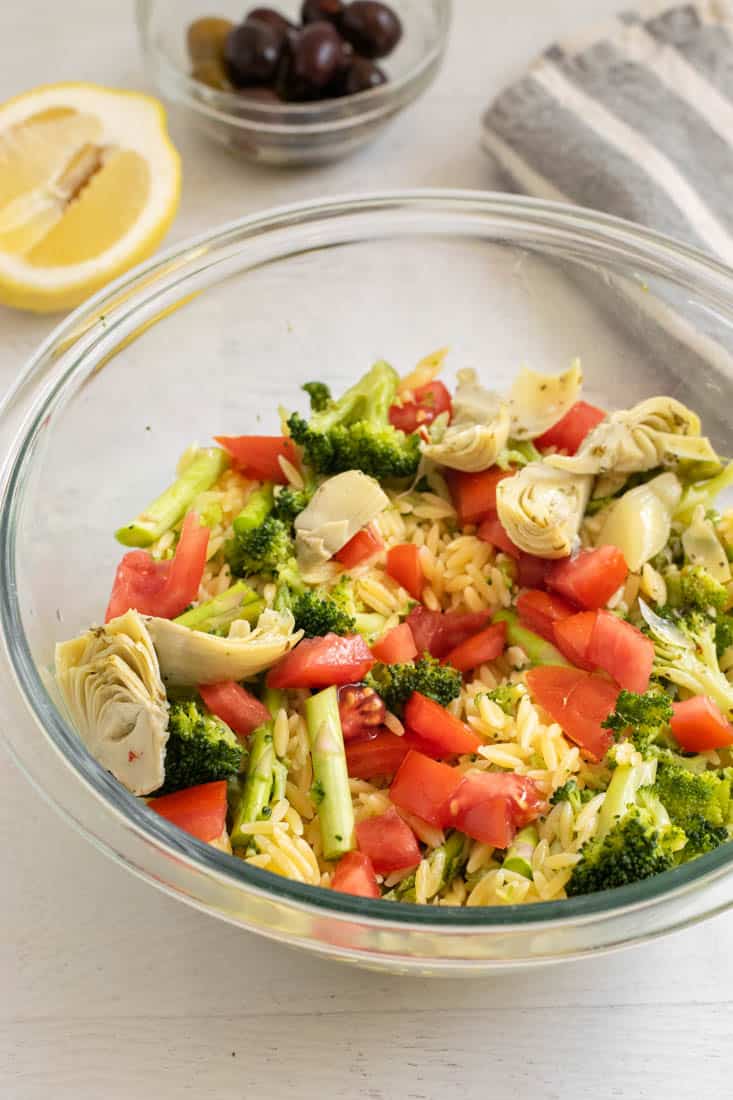 orzo salad with broccoli, tomatoes and artichokes in clear bowl