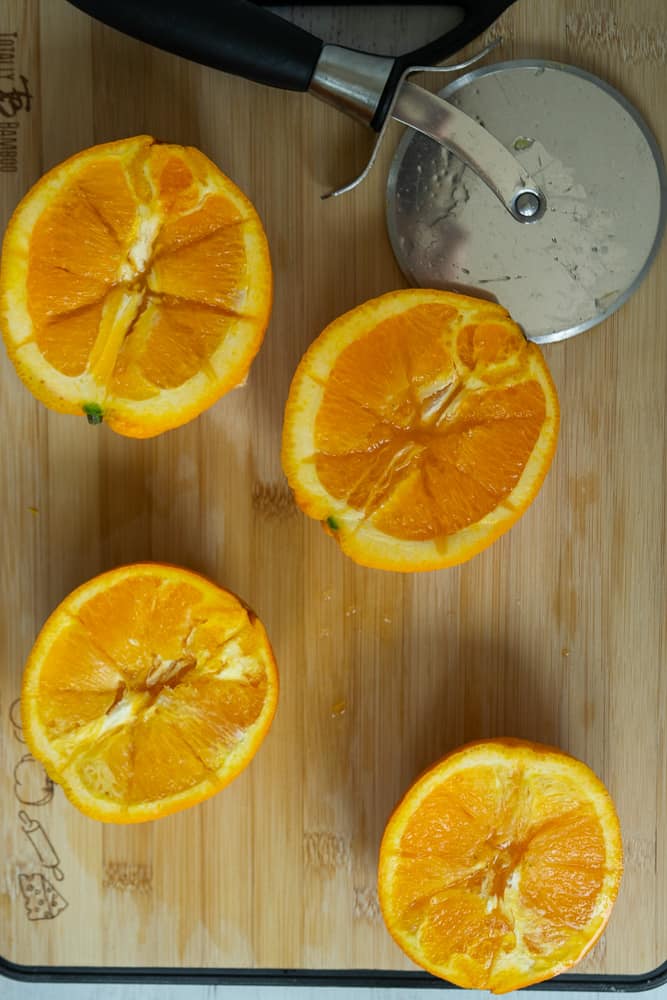 wooden cutting board with navel oranges and pizza cutter to slice flesh