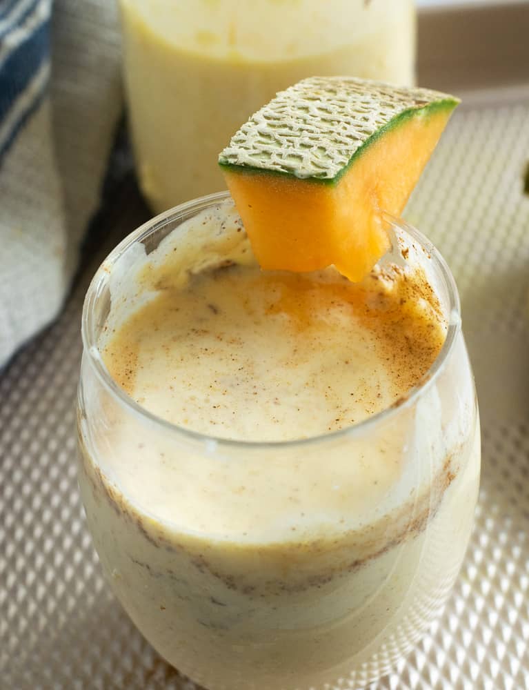 cantaloupe and mango smoothie with cantaloupe slice on glass