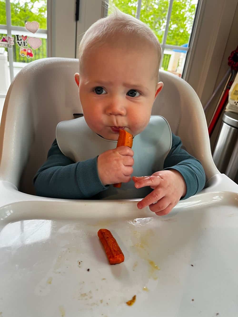 baby eating roasted carrots in high chair