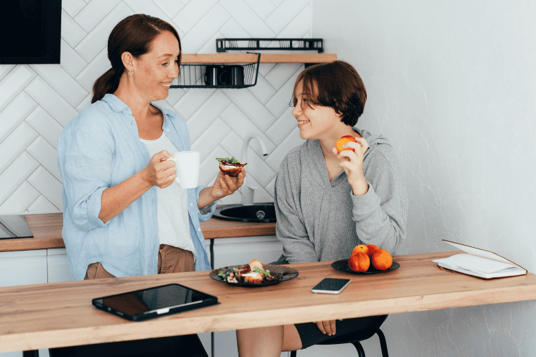 mom drinking coffee while son picks up piece of fruit