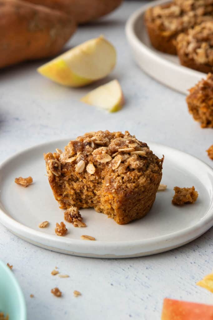 apple sweet potato muffin with oat crumb topping on white plate with bite taken out