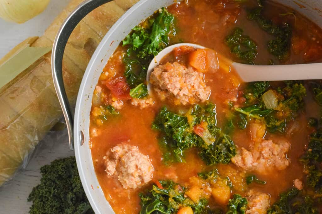 kale and meatball soup in pan with spoon