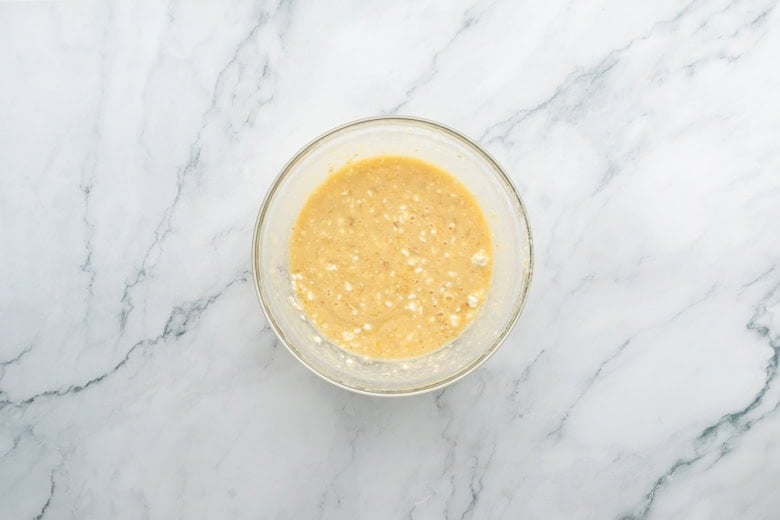Bowl of wet ingredients for cottage cheese and banana muffins on marble countertop surface.