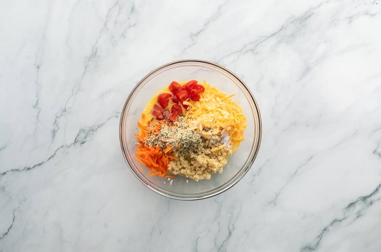 mixing bowl with quinoa, eggs, cheese, carrots, tomatoes to make quinoa egg muffins