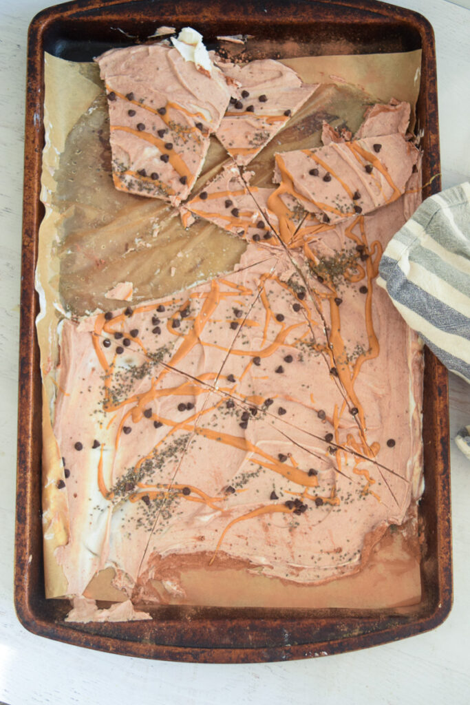 Frozen peanut butter chocolate greek yogurt bark broken into pieces on baking sheetpan with striped napkin alongside. 