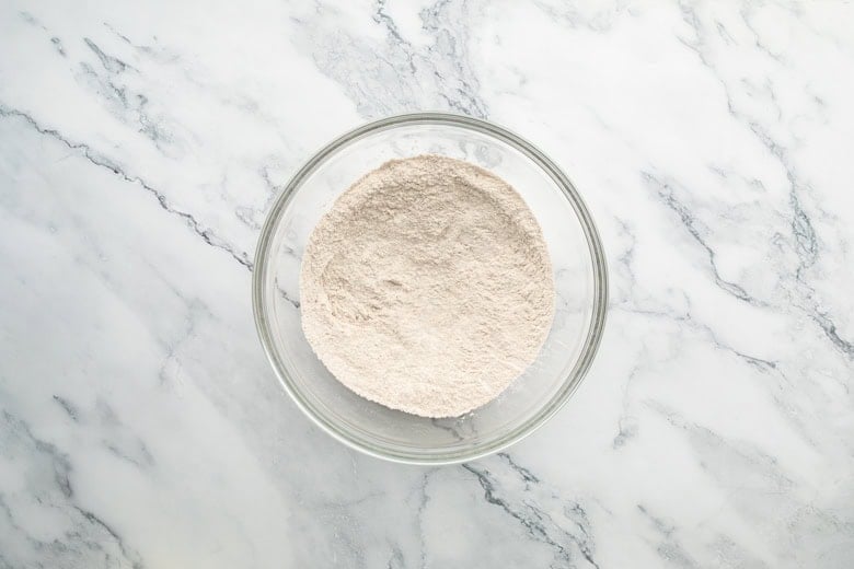 glass mixing bowl with dry ingredients, including flour, to make blueberry banana toddler muffins