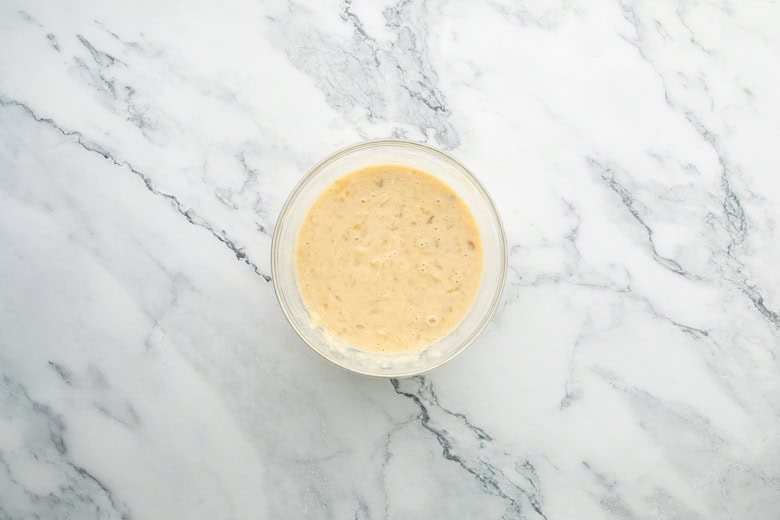 Homemade blueberry banana yogurt muffin batter in a glass bowl on marble surface, perfect for making delicious breakfast pancakes.