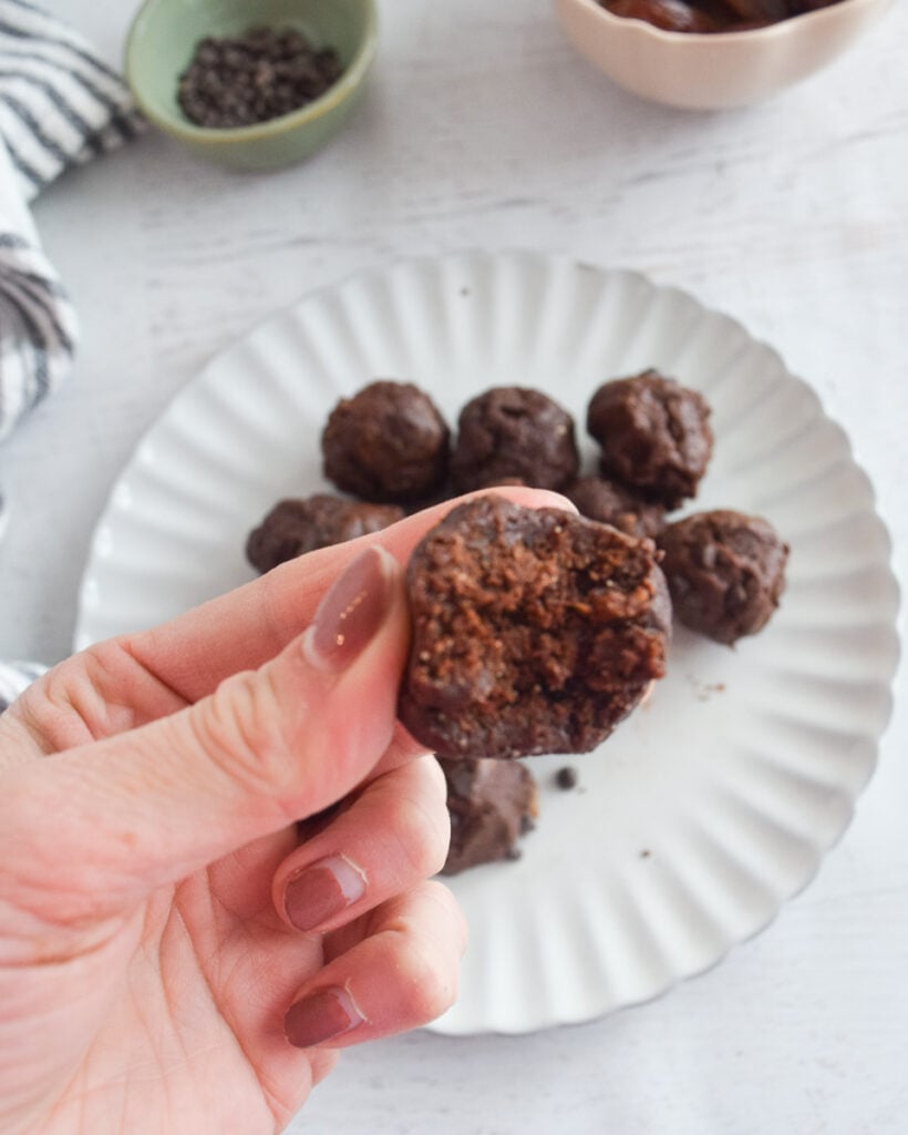 bite taken out of chocolate brownie bites made with dates with plate of more below