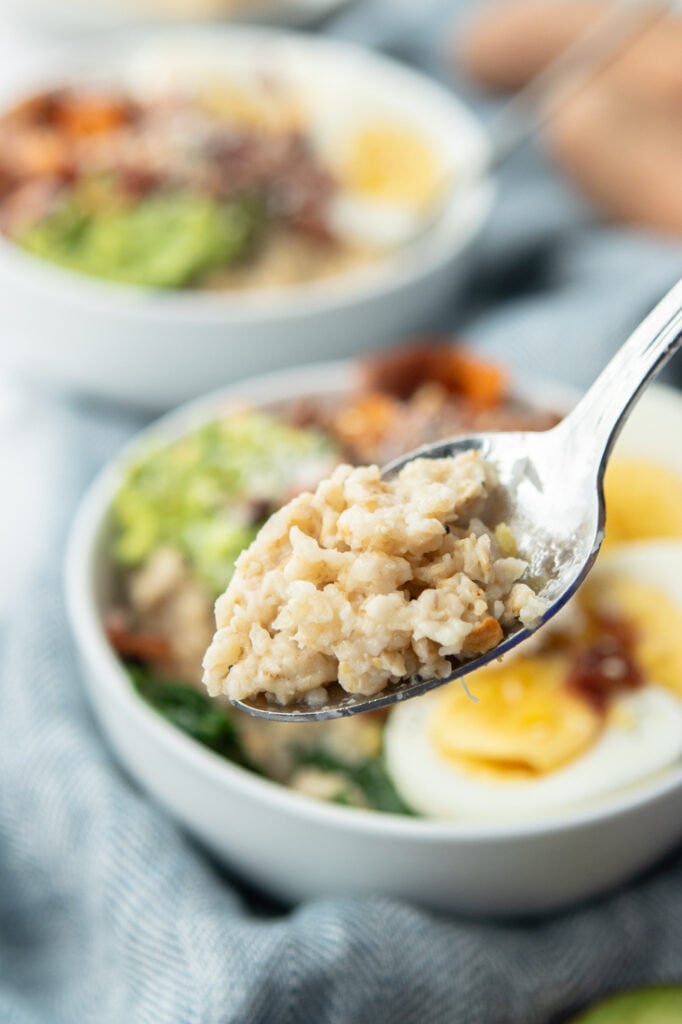 Spoon with savory oatmeal and spinach and rest of savory oatmeal bowl in background on blue napkin